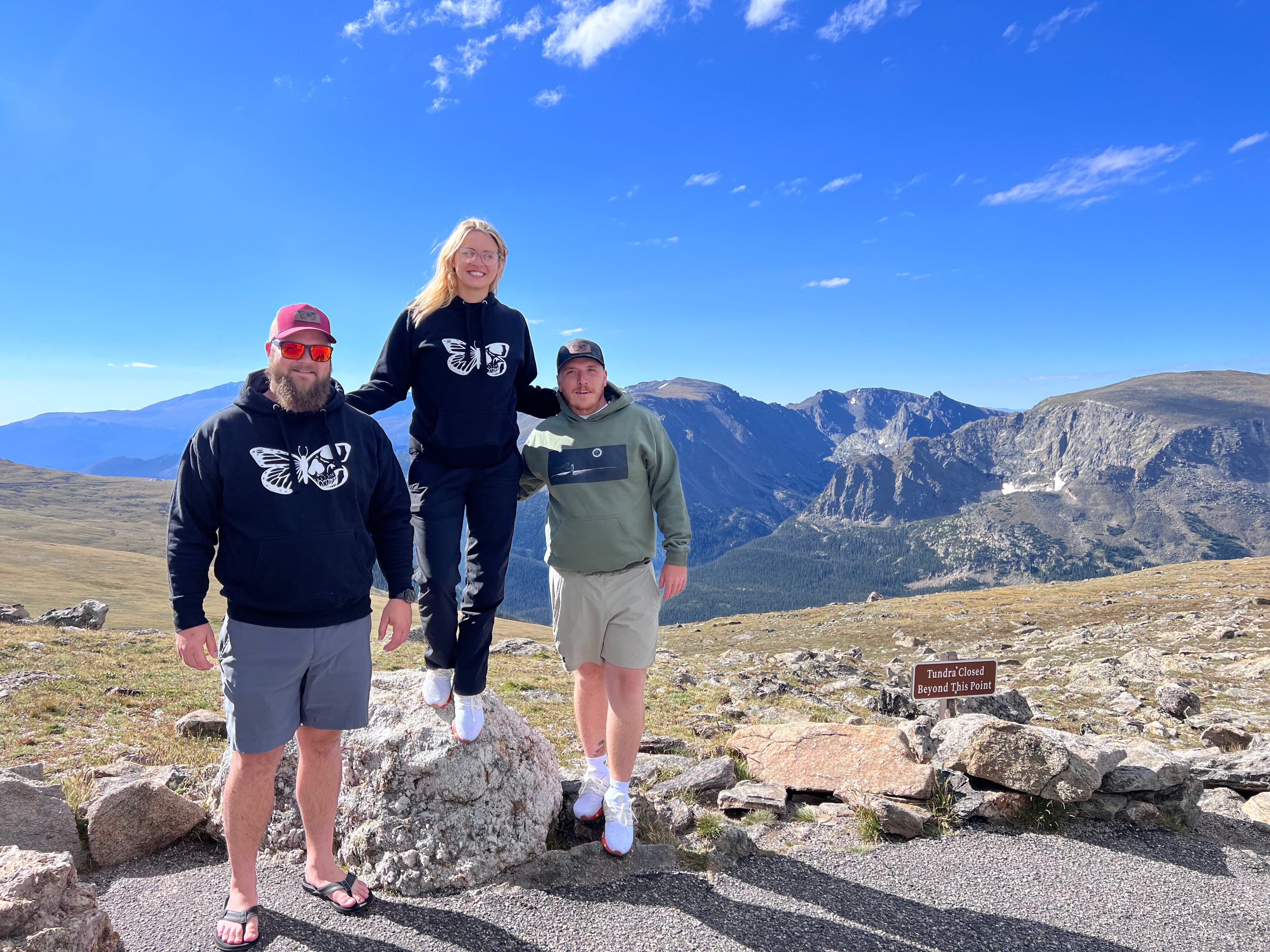 friends standing on mountain top with mountains and blue sky in background