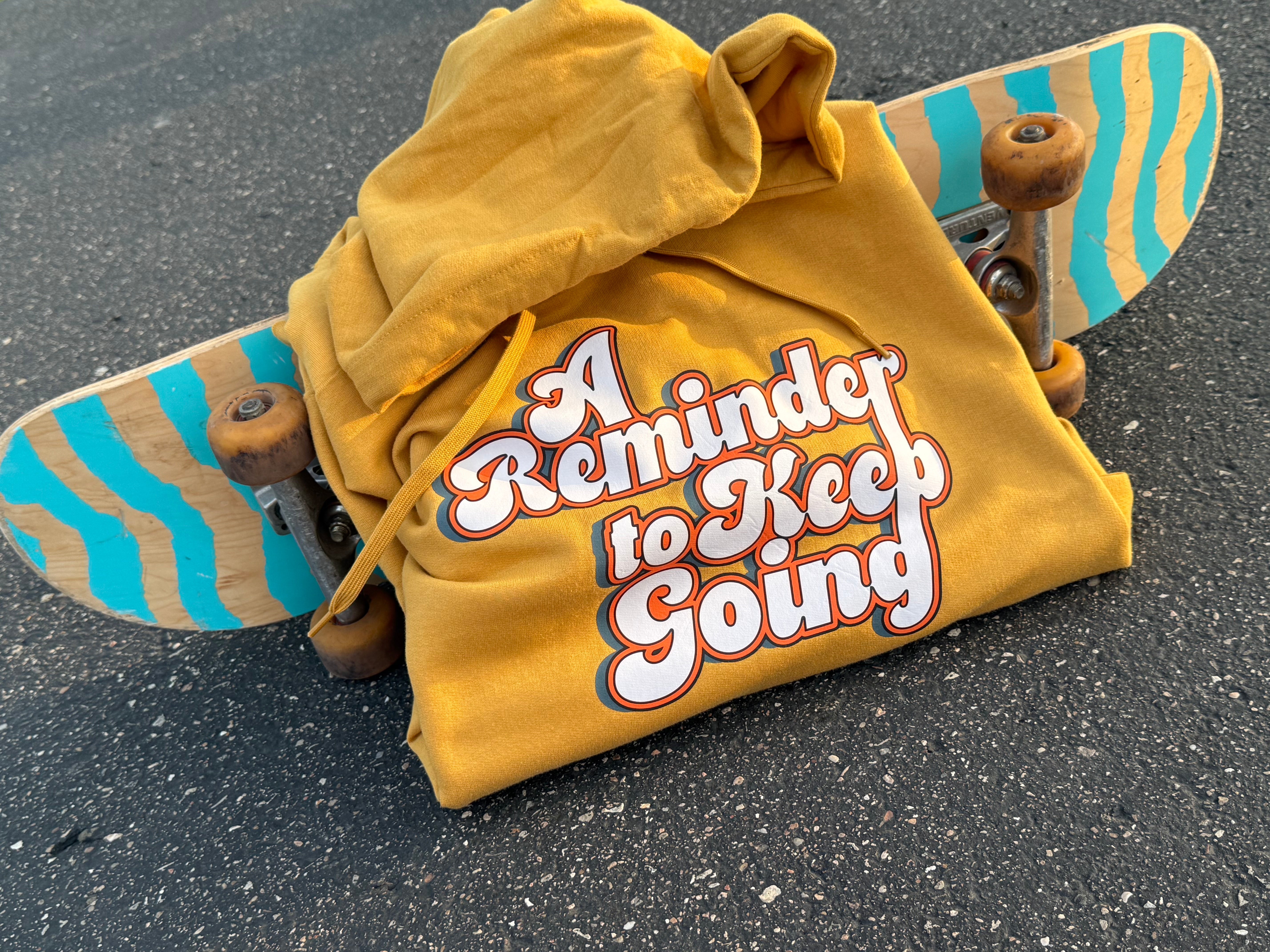 Yellow hoodie with 'A Reminder to Keep Going' text on a skateboard