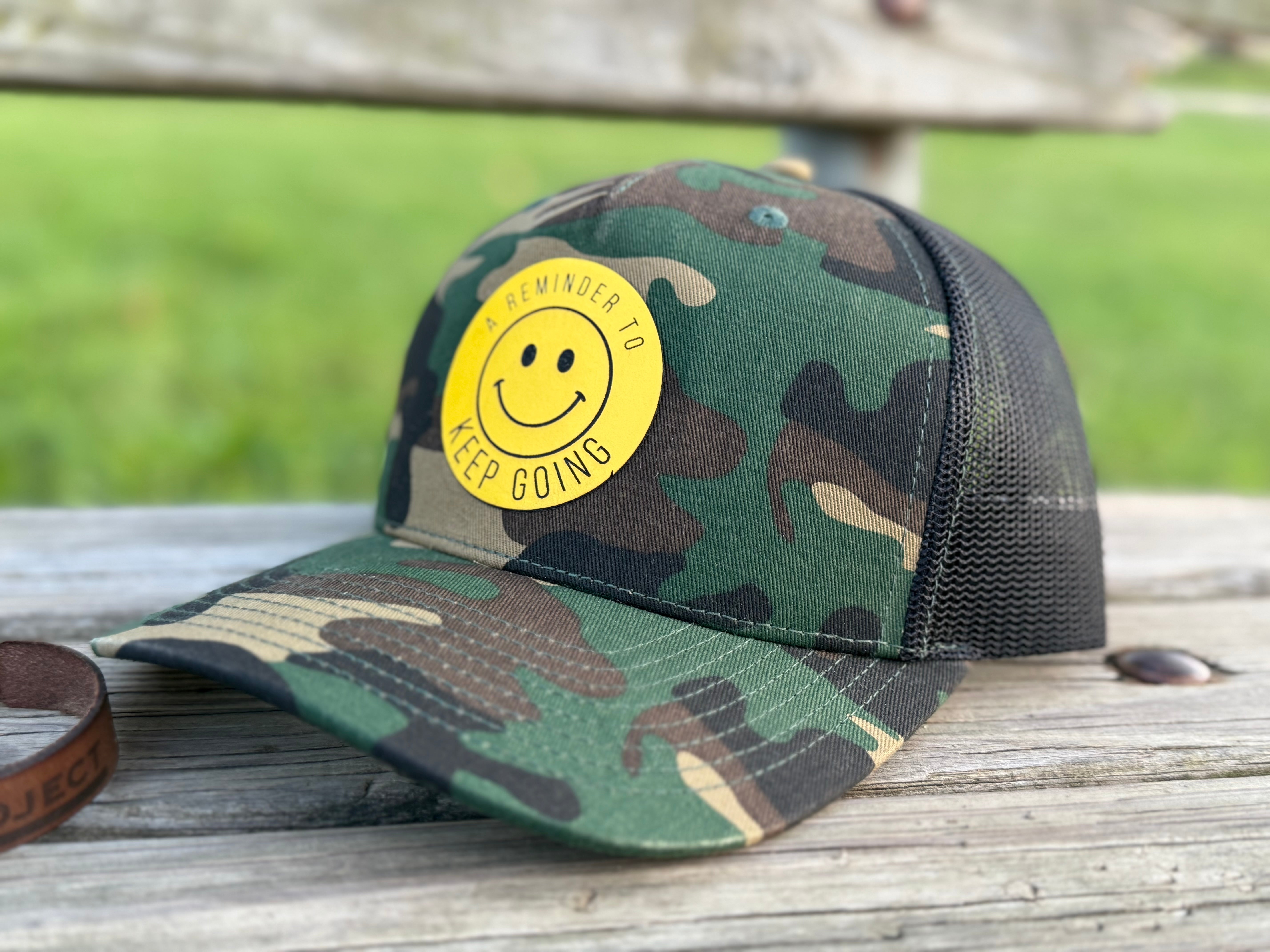 Camouflage cap with a yellow smiley face sticker on a wooden surface