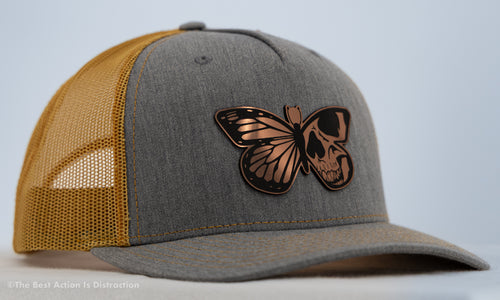 Gray and mustard yellow cap with a butterfly skull design on a light gray background