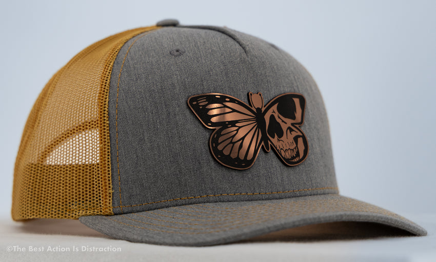 Gray and mustard yellow cap with a butterfly skull design on a light gray background