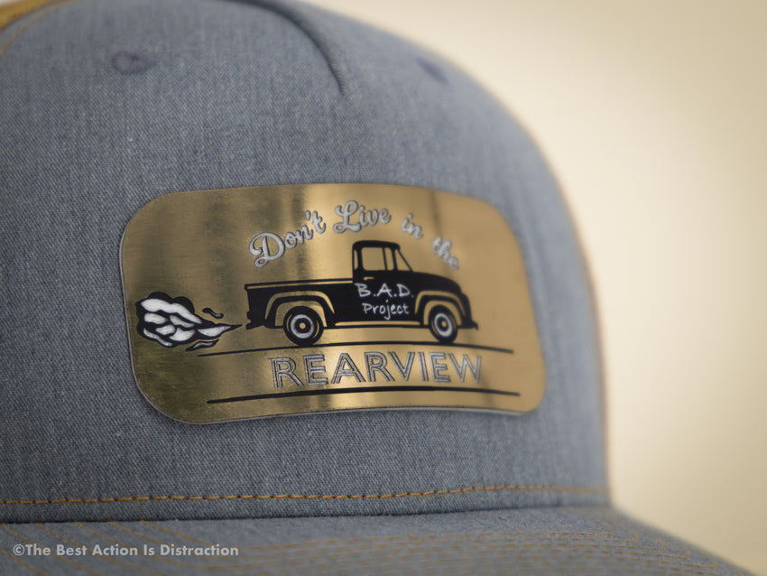 Gray cap with a brass emblem featuring a truck and text on a blurred background