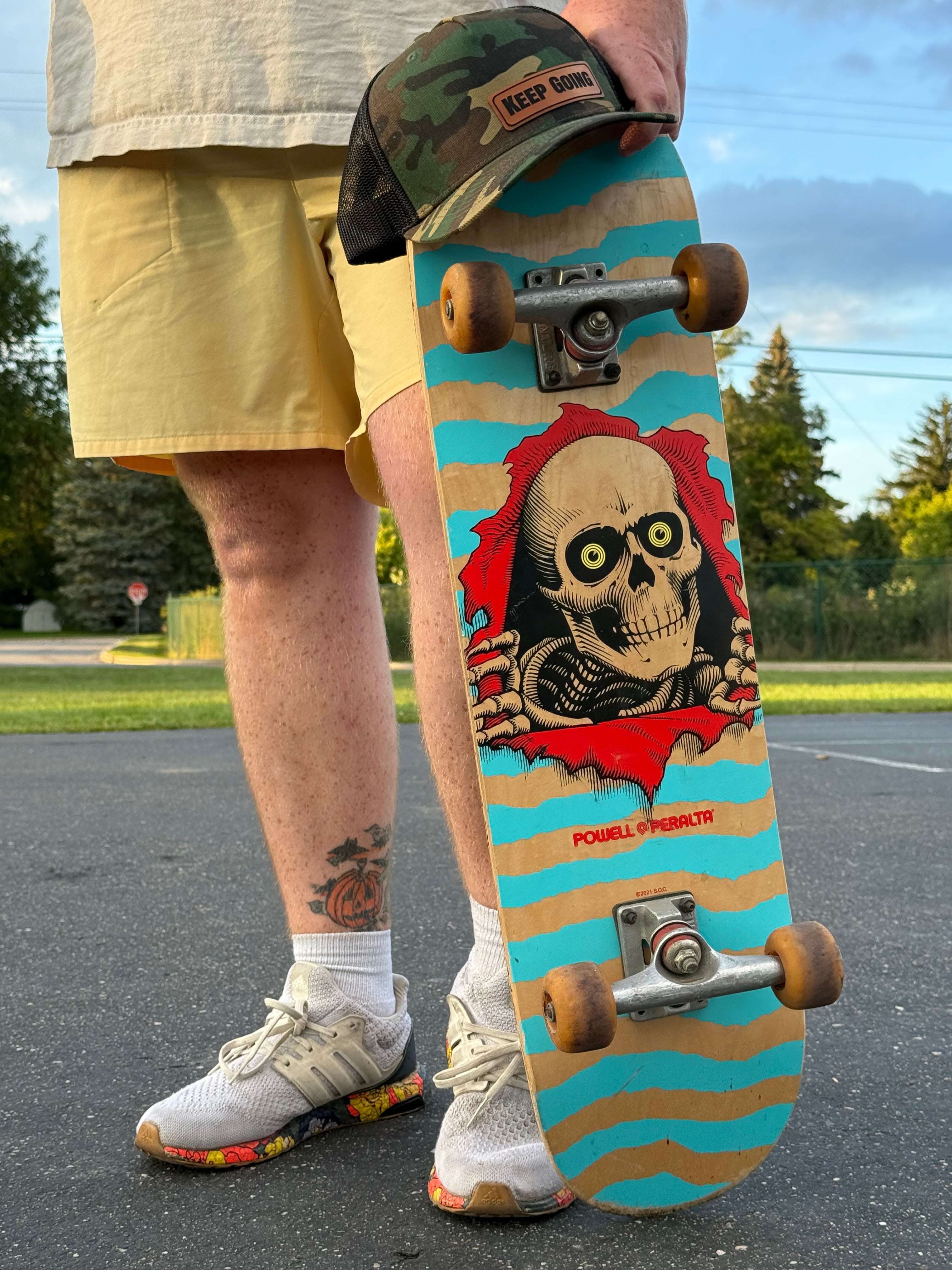 Person holding a skateboard with a skull design on a road