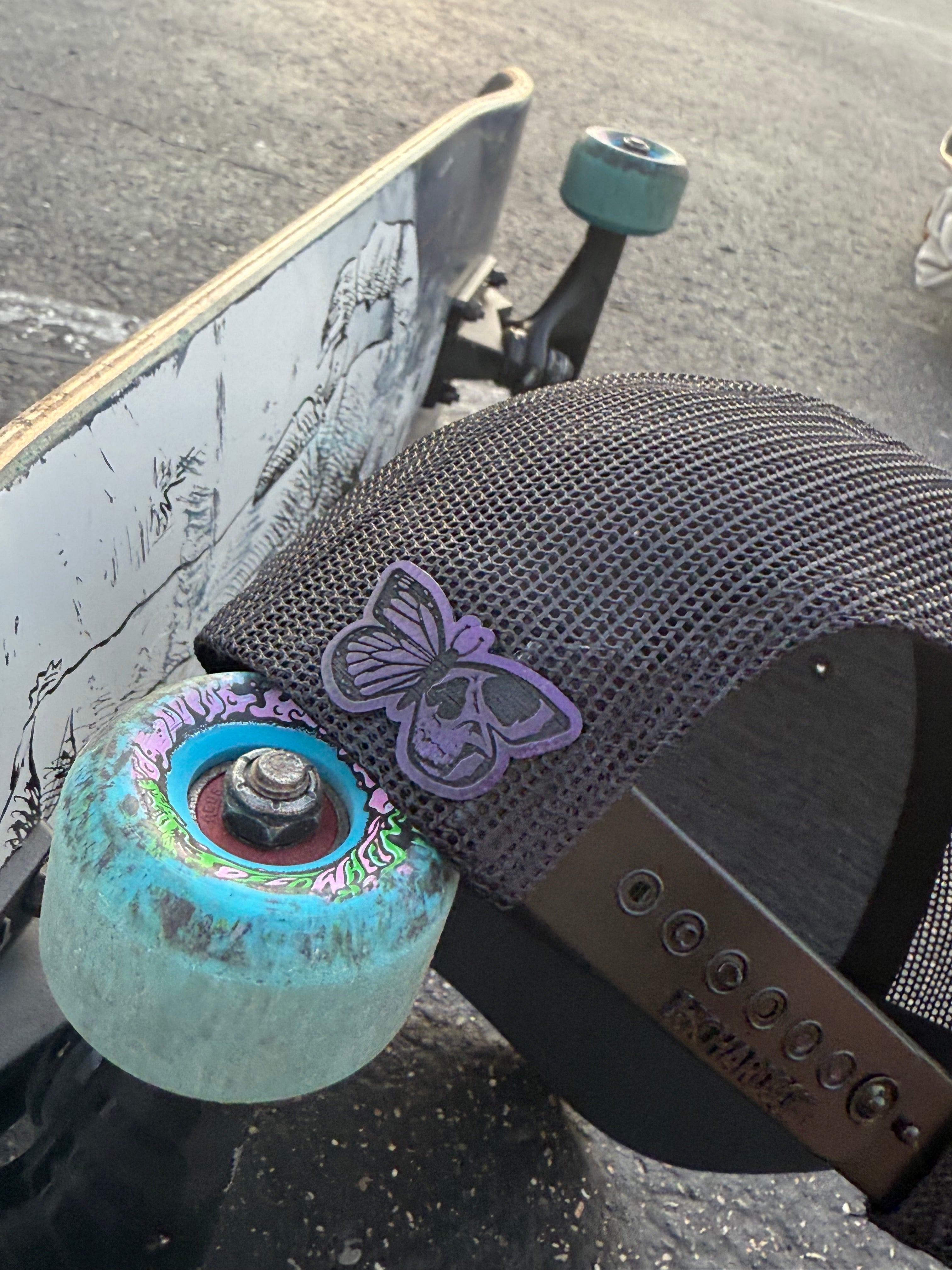 Close-up of a skateboard with a purple butterfly design on the truck, on a concrete surface.