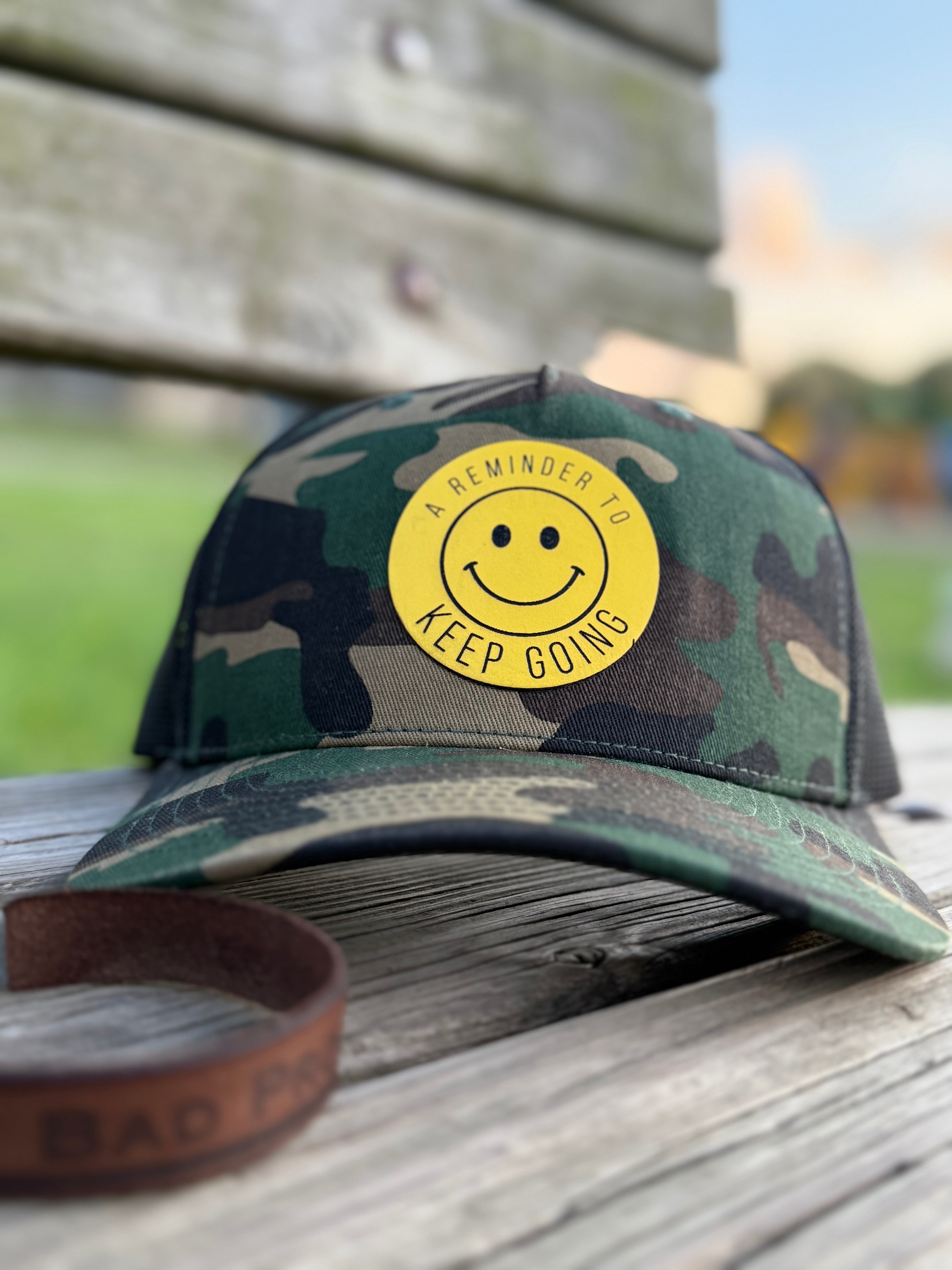 Camouflage cap with a yellow smiley face sticker on a wooden surface