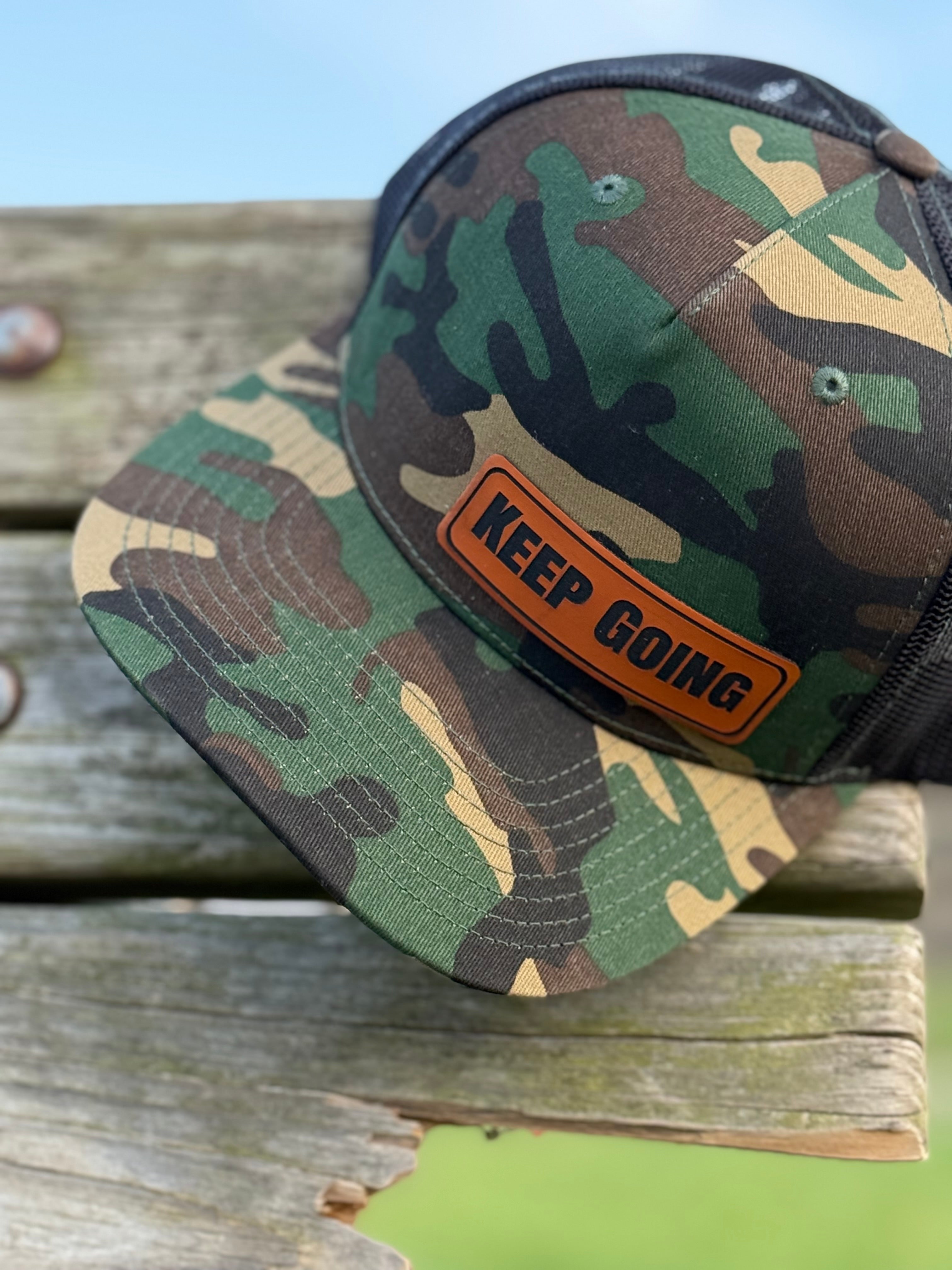 Camouflage cap with 'Keep Going' patch on a wooden surface