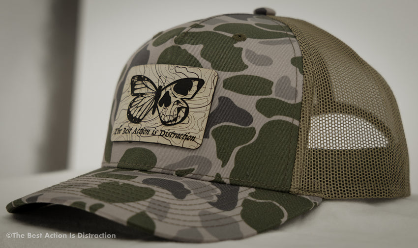 Camouflage cap with a butterfly design and text on a neutral background